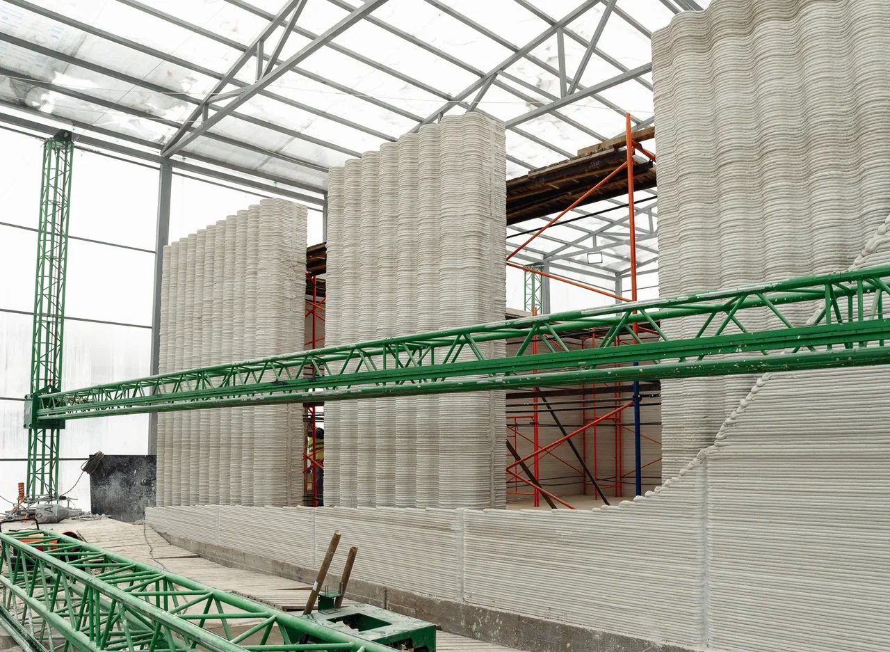 The 3D-Printed Medical Clinic — large-format 3D printer building a curved concrete wall inside an enclosure